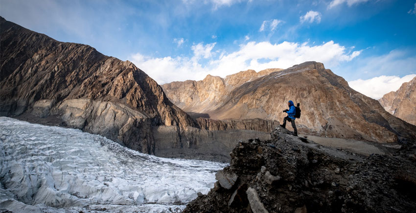 person wearing blue jacket and holding a camera is standing a mountain in Pakistan